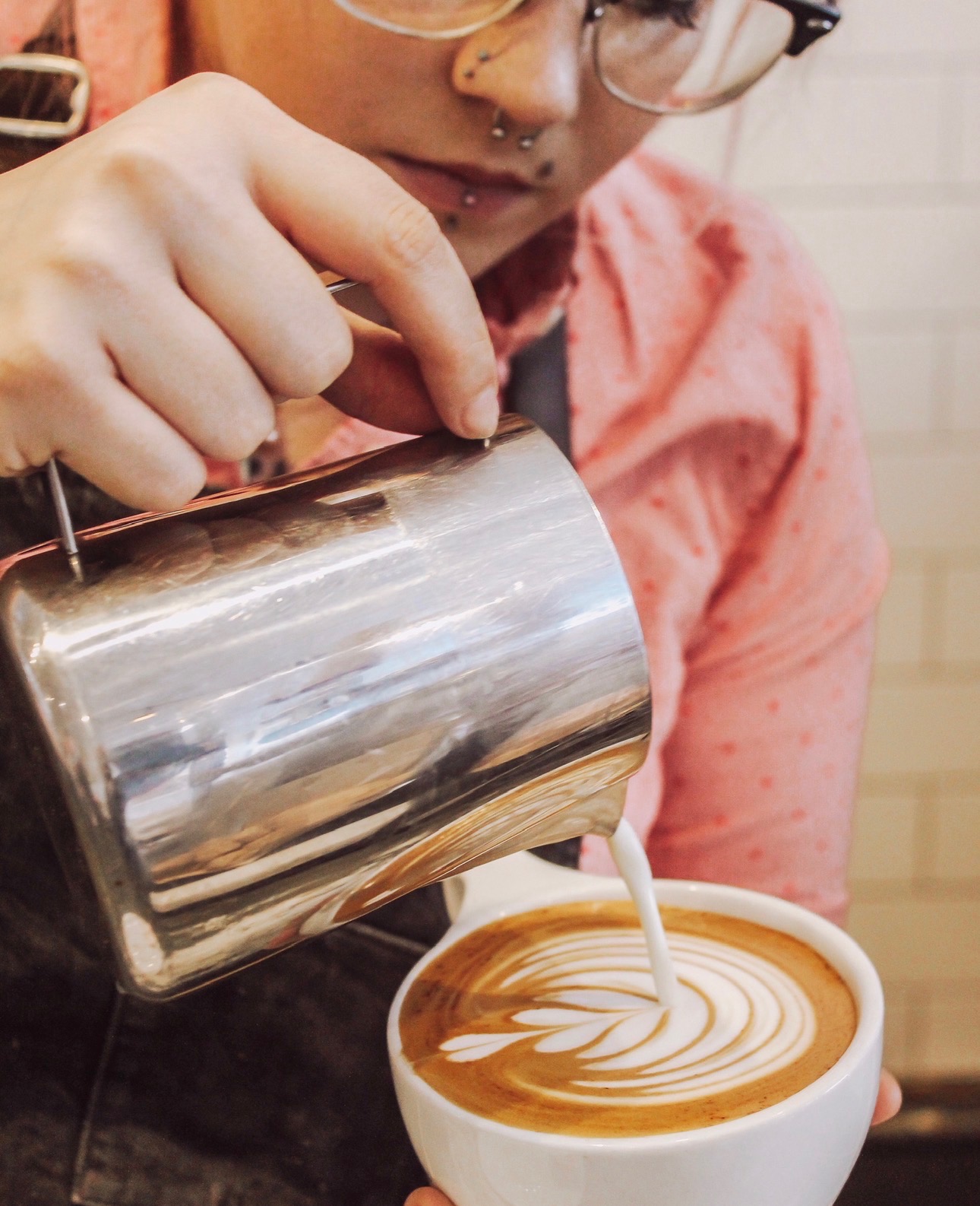 Close-up picture of steamed milk being poured from a silver pitcher into a white mug to create latte art.